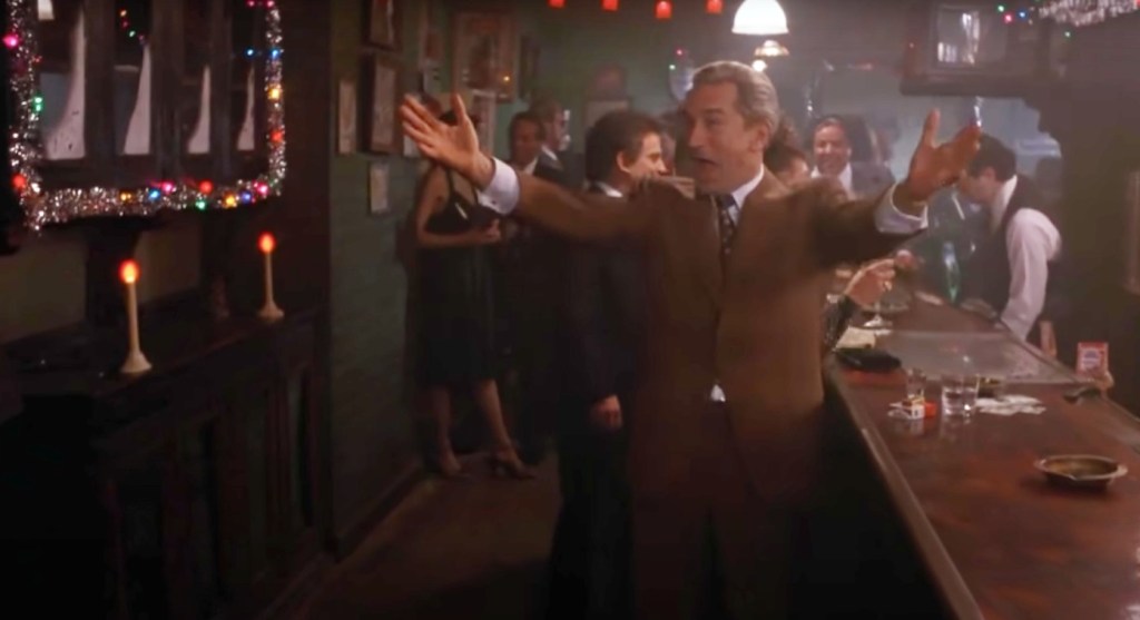 Robert De Niro as Jimmy Conway in Goodfellas, with open arms and a smile at the Christmas party