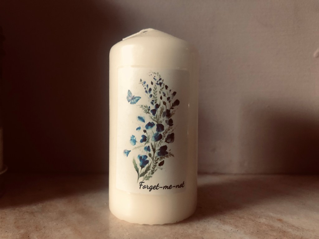 White candle with 'Forget-me-not' on the front.